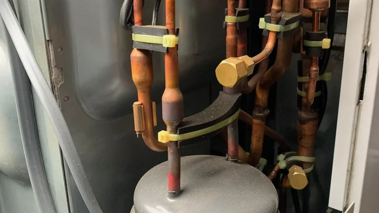 Interior view of a heat-pump outdoor unit showing copper refrigerant pipes and compressor