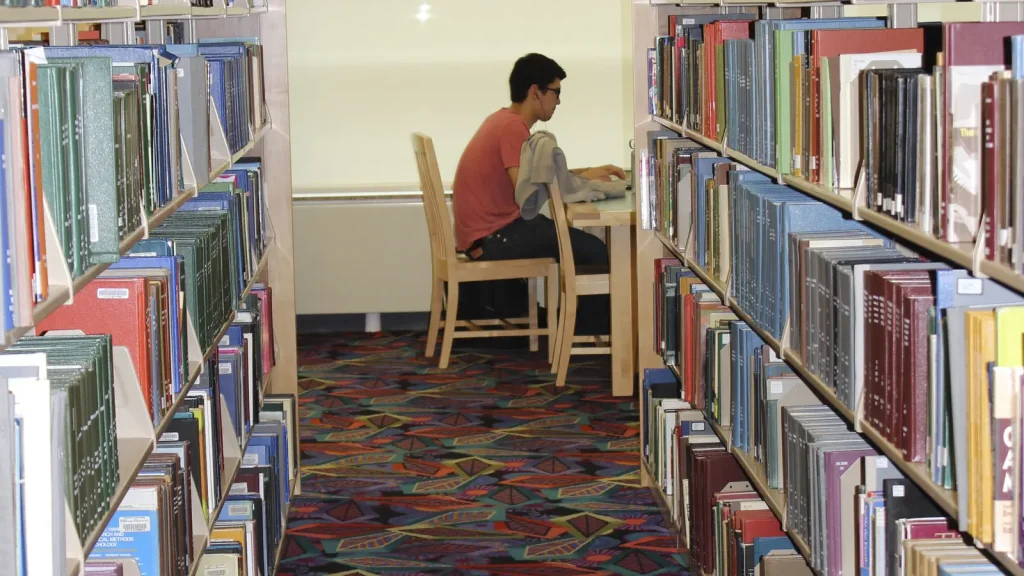 A university student reading and taking notes at a library desk