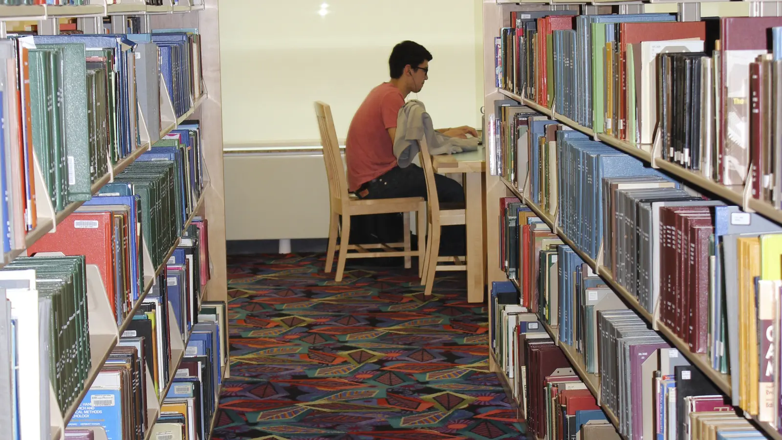 A university student reading and taking notes at a library desk