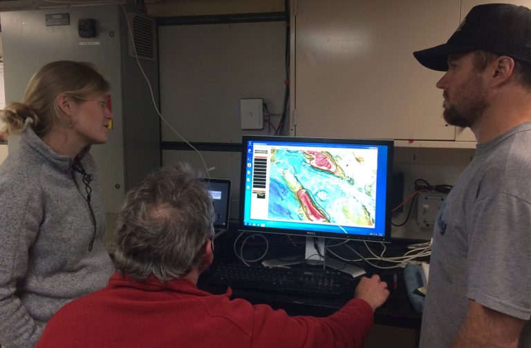 Three geophysicists discussing a detailed seafloor map on a computer