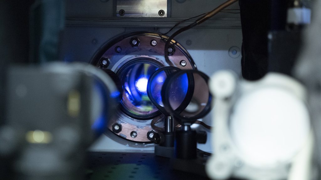 Blue light shining from the circular chamber of a NIST strontium optical atomic clock