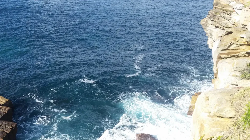 Blue-green ocean waves breaking below a rocky coastal lookout