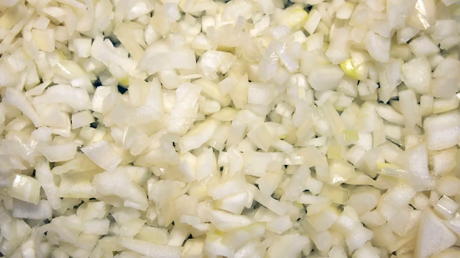 Close-up photograph of freshly chopped white onion pieces on a cutting surface