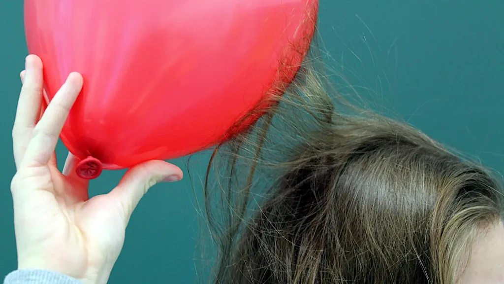 Child demonstrating static electricity as charged hair rises toward a balloon