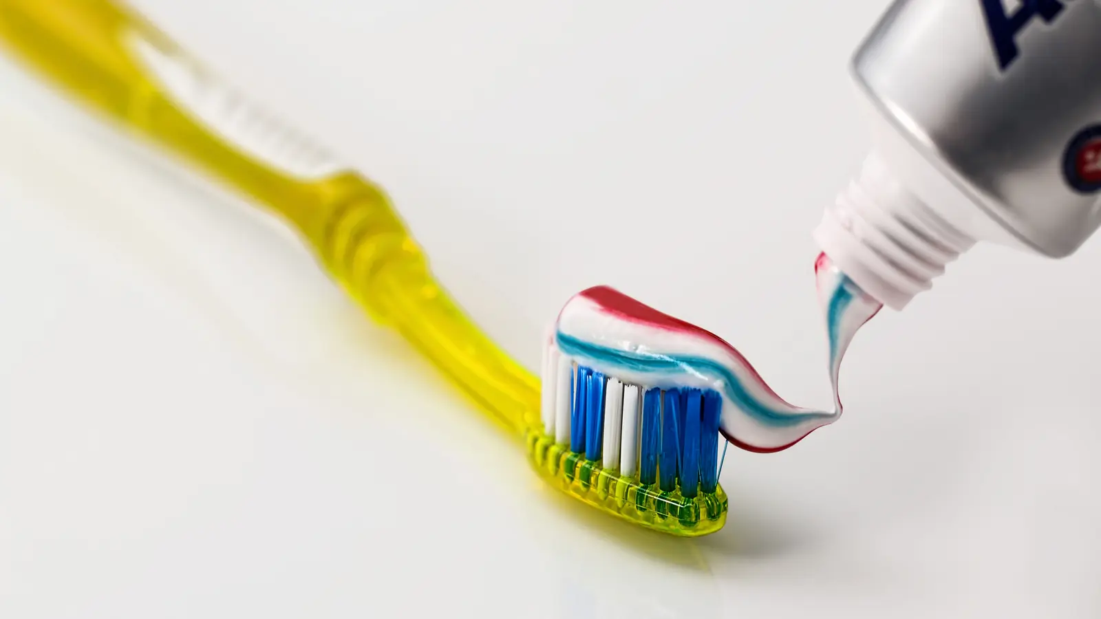 Toothbrush beside an open tube of white toothpaste on a clean surface