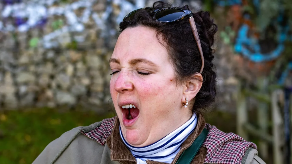 Woman covering her mouth while yawning outdoors